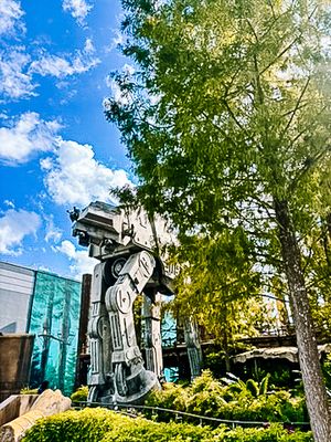 AT-AT Walker sculptures among trees create a Star Wars themed outdoor display against a bright blue sky.