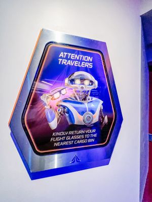 Futuristic blue illuminated warning sign showing a robot figure requesting travelers to return flight glasses at a space station.