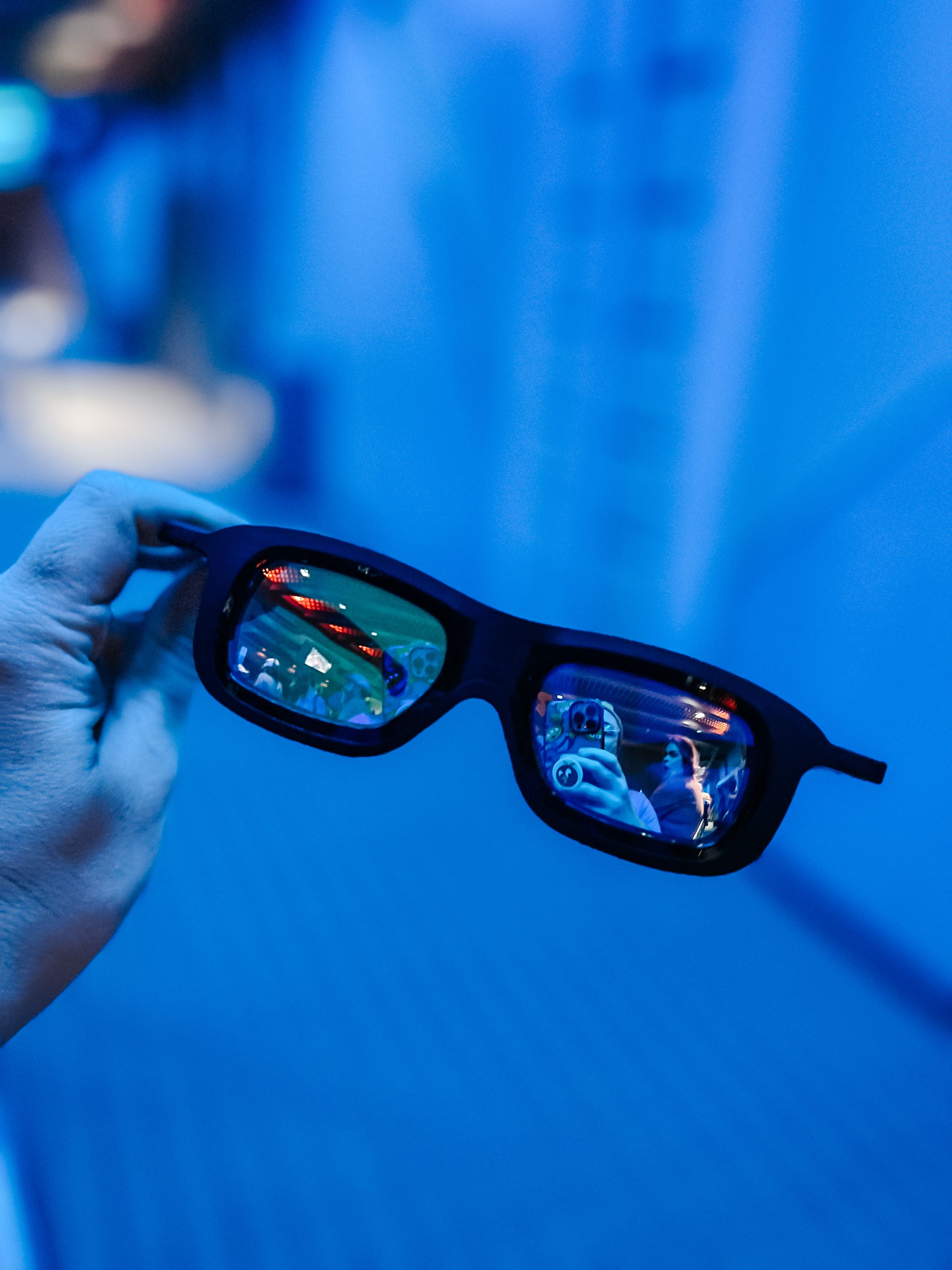 Black sunglasses held against a vibrant blue background showing reflective lenses with distorted figures.