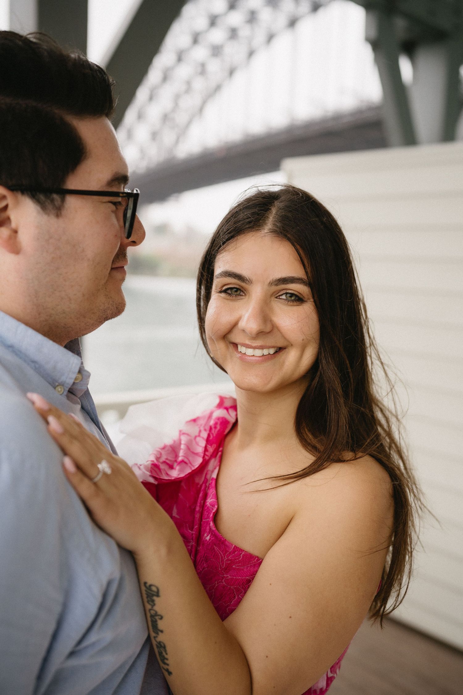 A romantic couple embraces under an architectural structure wearing a pink dress and blue shirt.