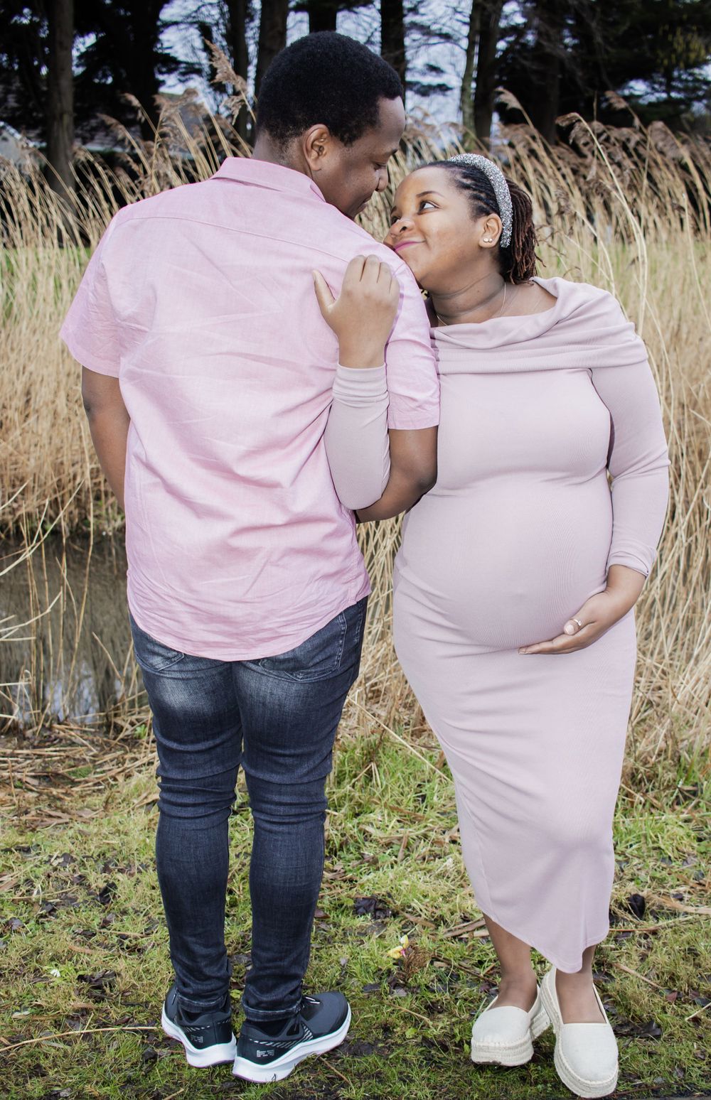 Beautiful maternity photo of a couple in matching pink outfits standing together in a field of tall grass.