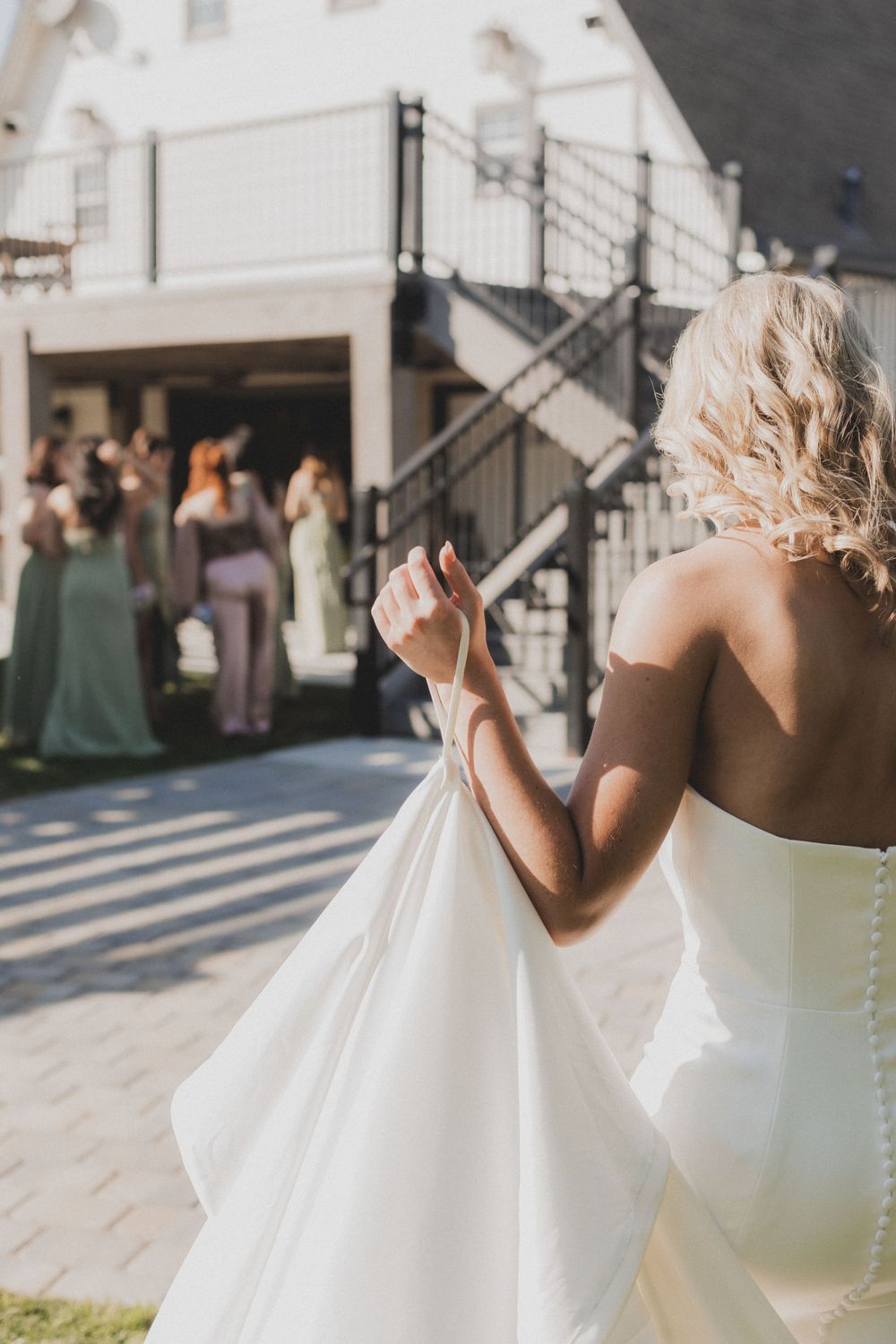 Back view of a bride in a white strapless gown standing outside a white barn venue.