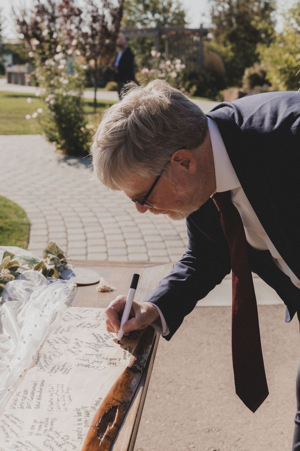 Someone signing a guest book at an outdoor event with autumn trees in the background.