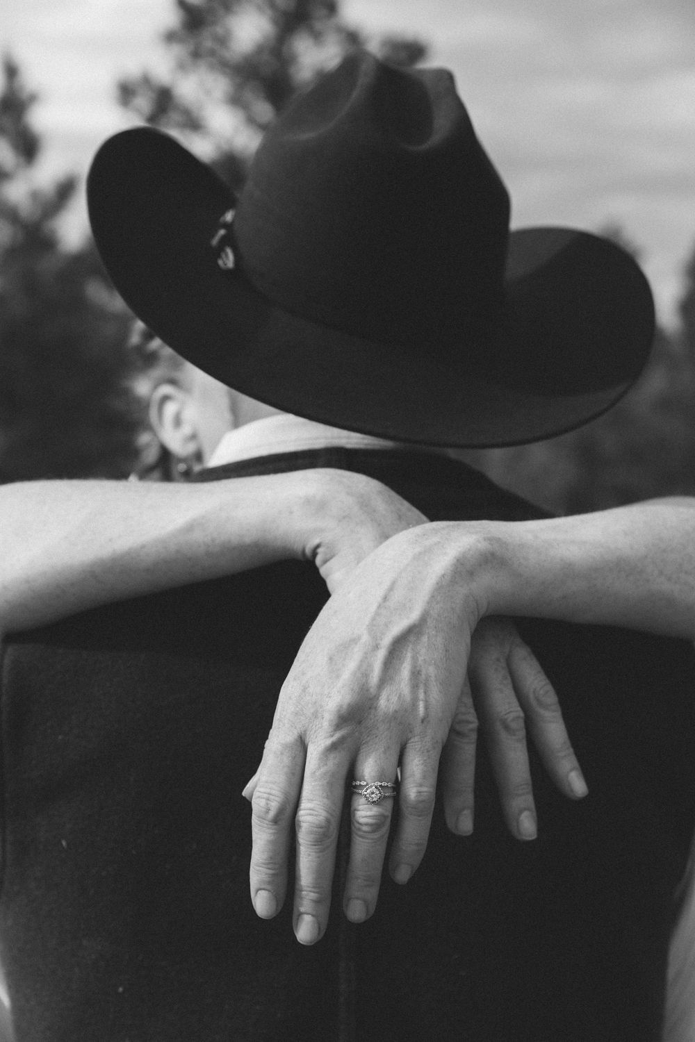 Close-up black and white photo showing hands with wedding rings resting on formal attire.