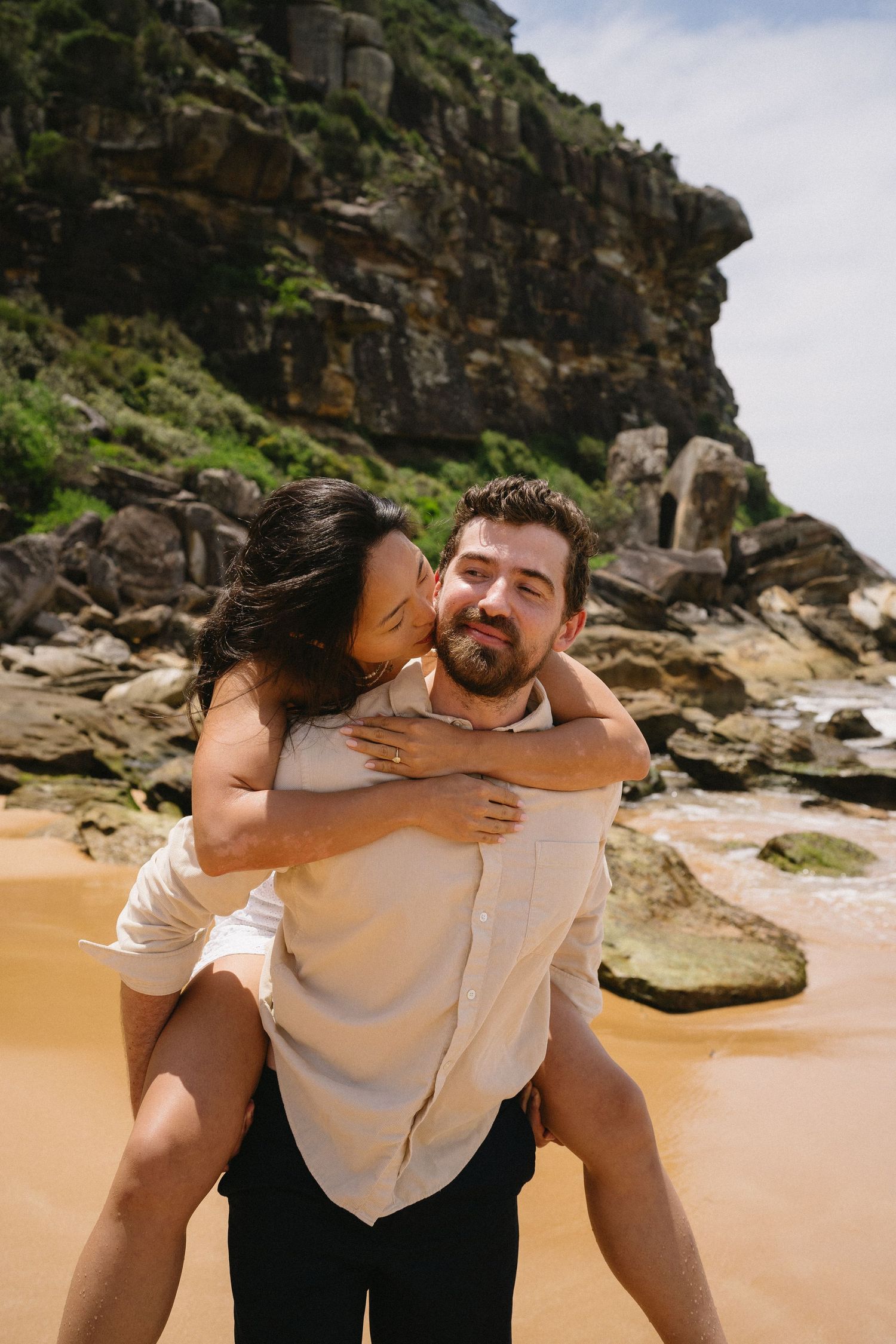 A joyful moment shared between a couple on a beach with dramatic cliffs in the background.
