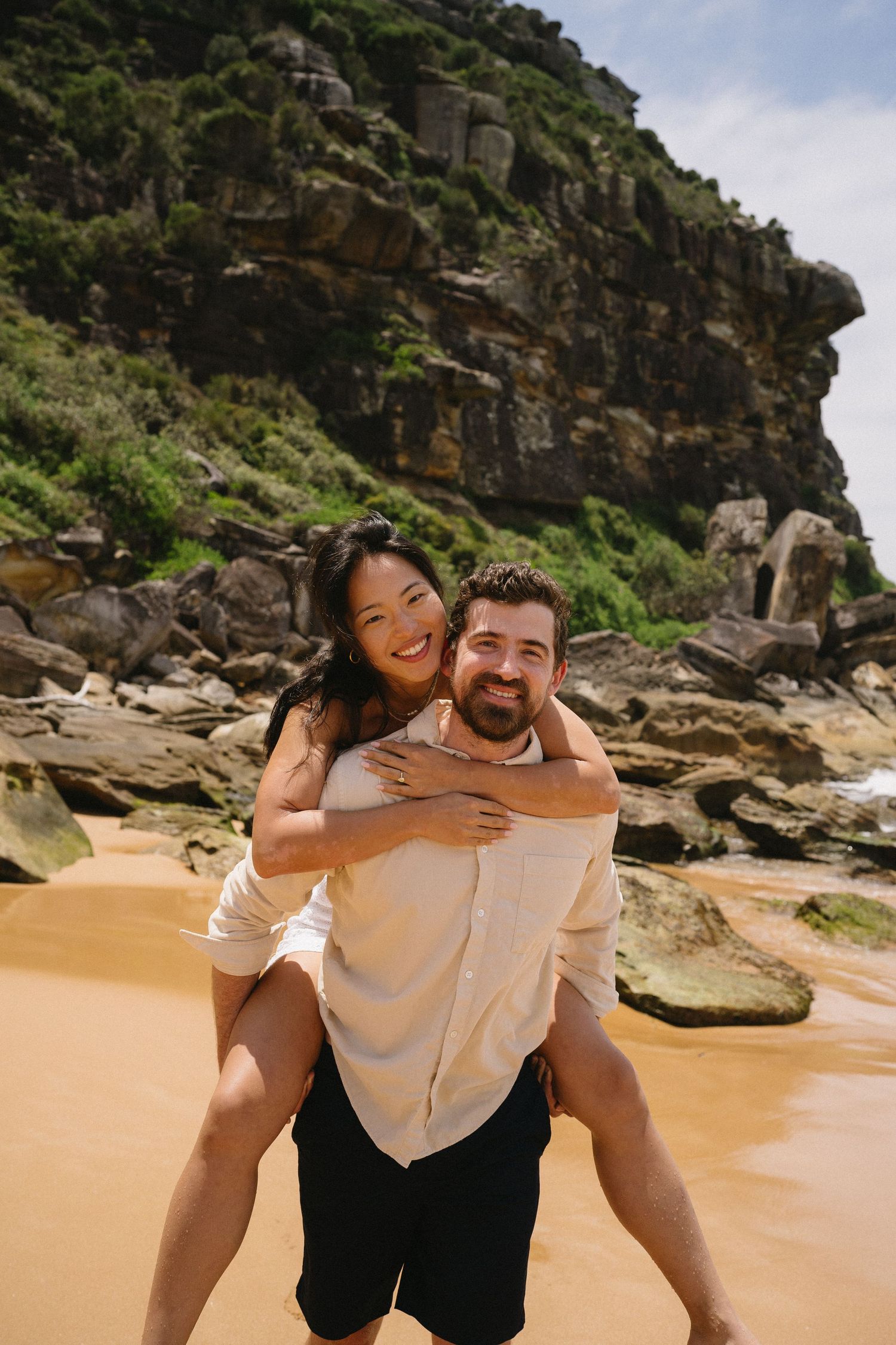 A couple shares laughter during a playful piggyback ride on a scenic beach.