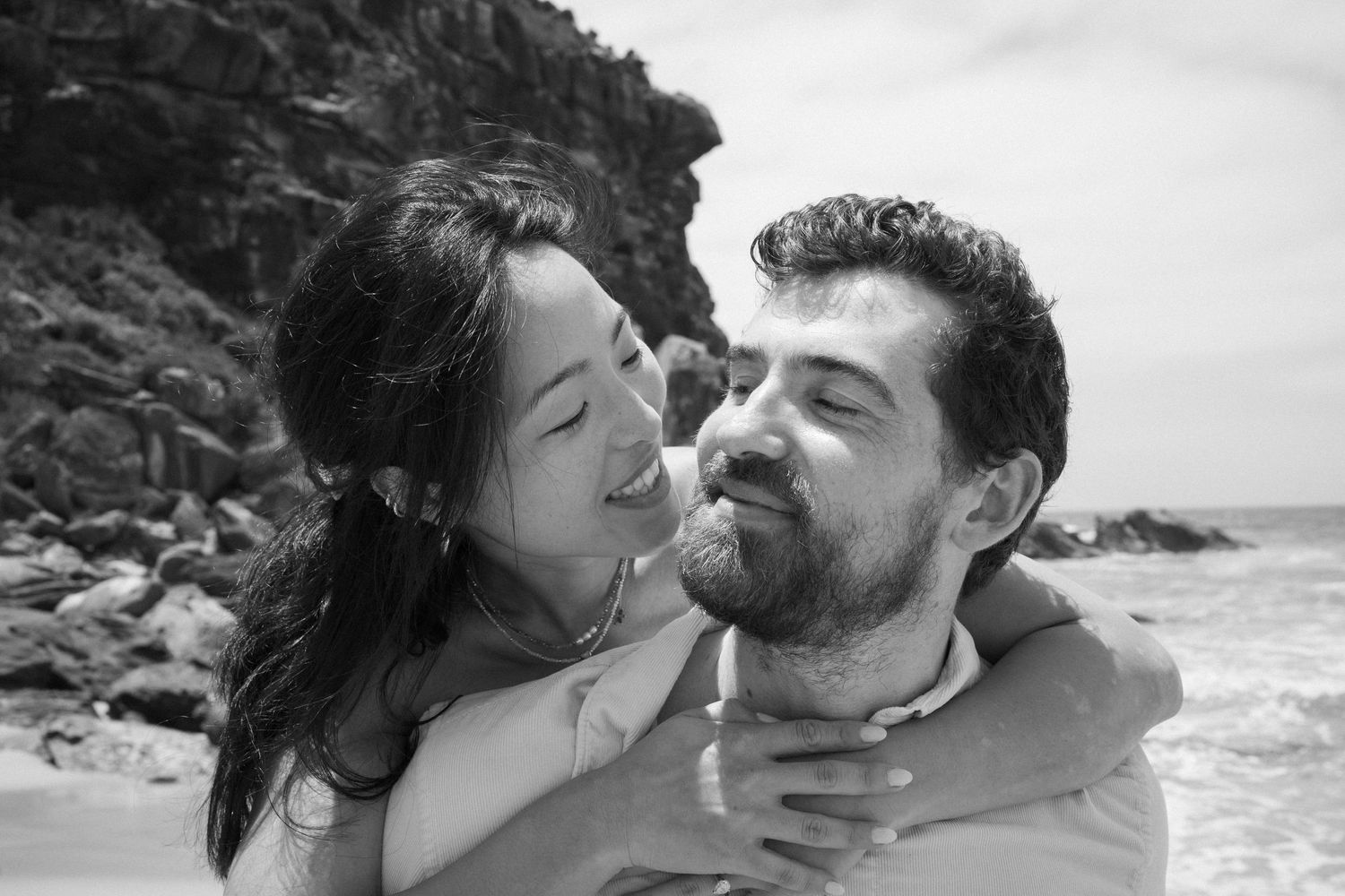 An intimate black and white portrait of a couple sharing a tender moment by the ocean.