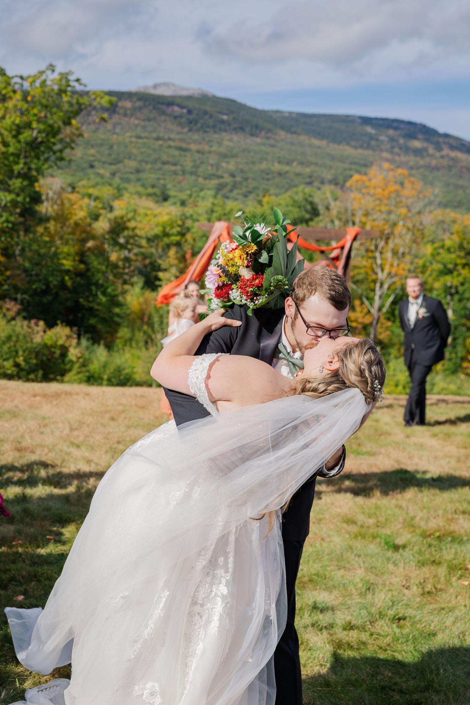 A romantic dip kiss during a mountaintop wedding ceremony with fall foliage in the background.