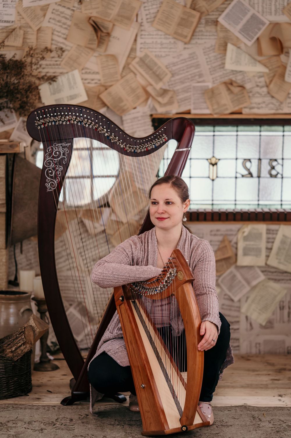 Woman sitting with an ornate harp in a room decorated with floating sheet music pages.