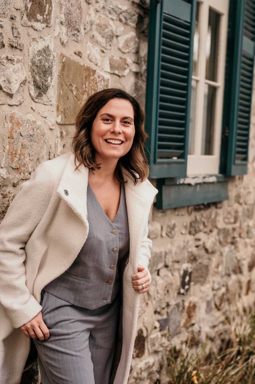 Classic neutral outfit styled against stone wall with green shutters.