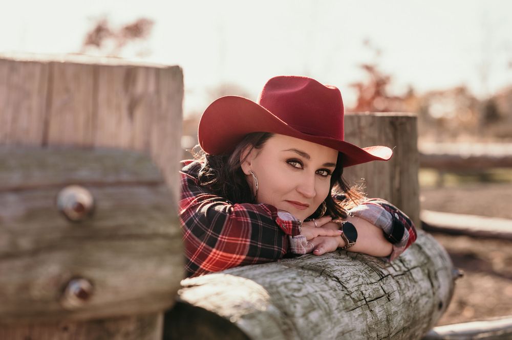 Western style scene with red cowboy hat and plaid scarf against wooden fence.