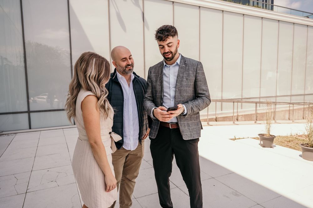 Professional colleagues gathered outdoors near modern office building reviewing information on mobile devices.