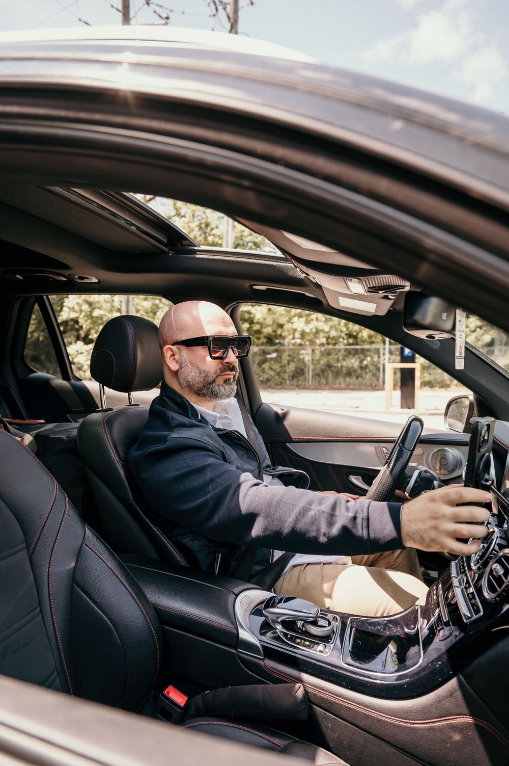 A man in business attire sitting in the driver's seat of a luxury car, adjusting vehicle controls.