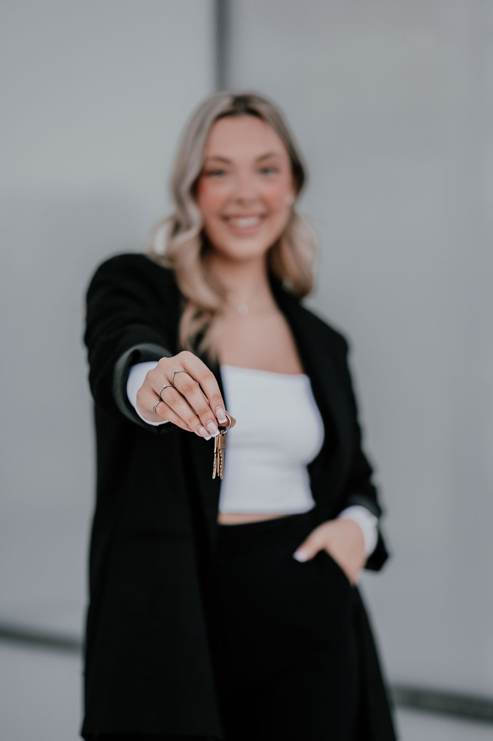 Professional holding up keys while wearing black blazer against grey wall.