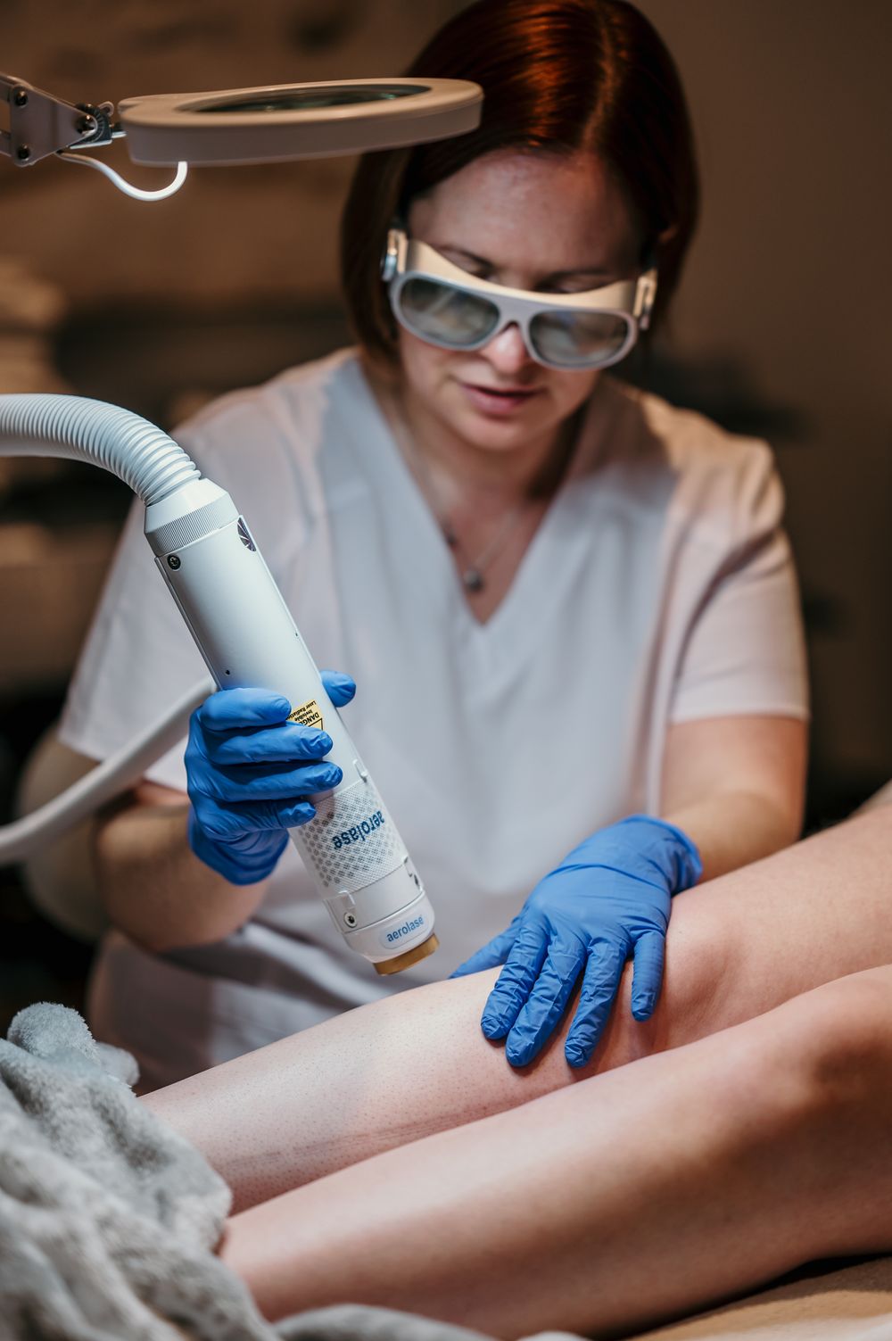 Medical professional in protective gear performing laser hair removal treatment on a client's leg.