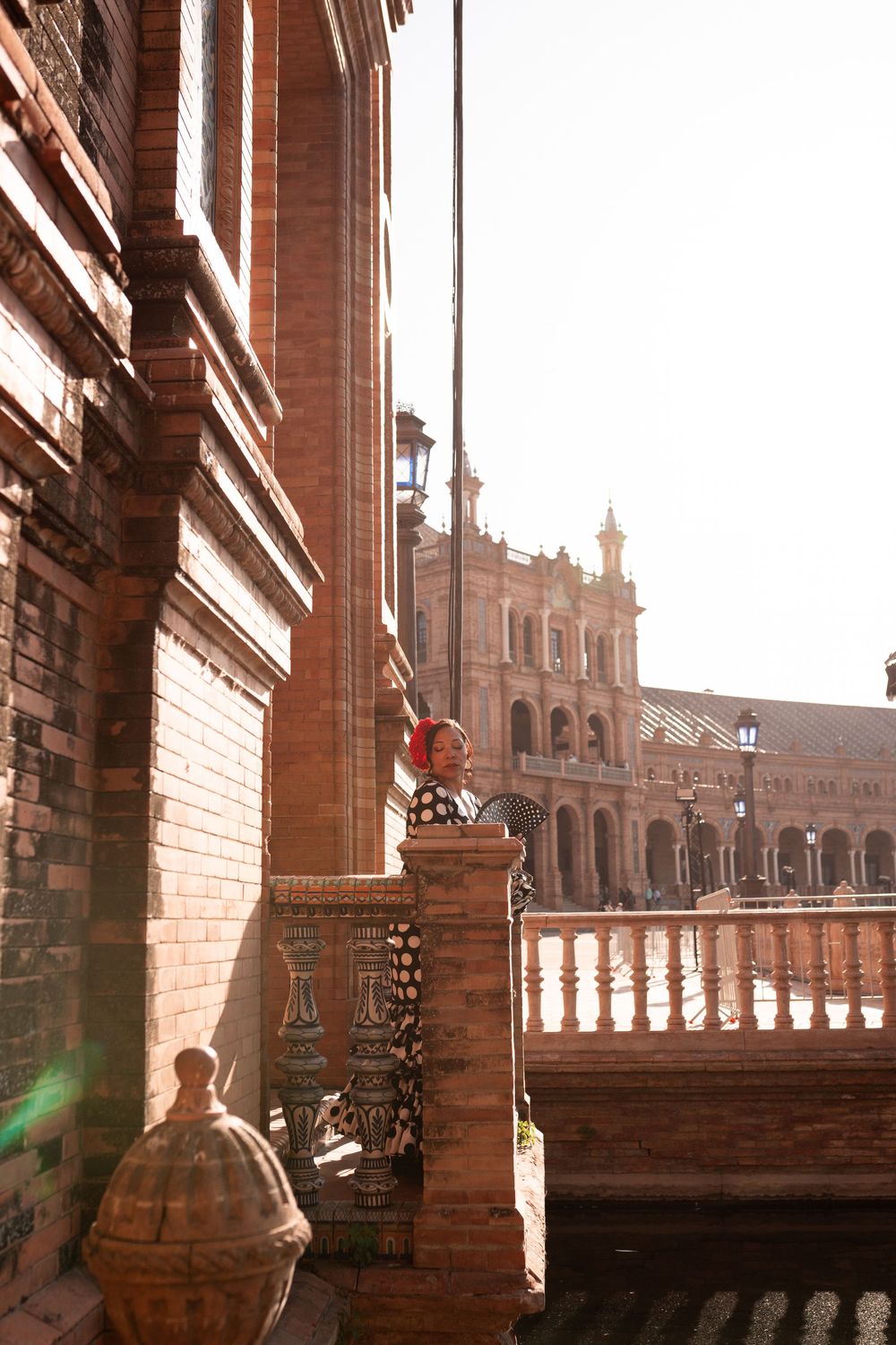 Woman in flamenco dress stands by ornate brick colonnade at Plaza de España, Seville.
