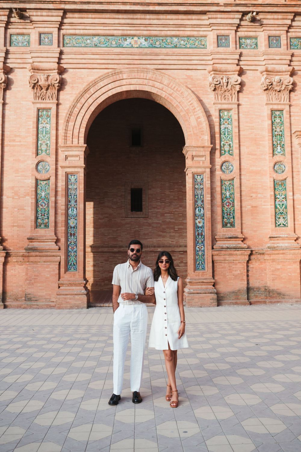 Couple posing in front of detailed tilework and arches at Plaza de España in Seville.