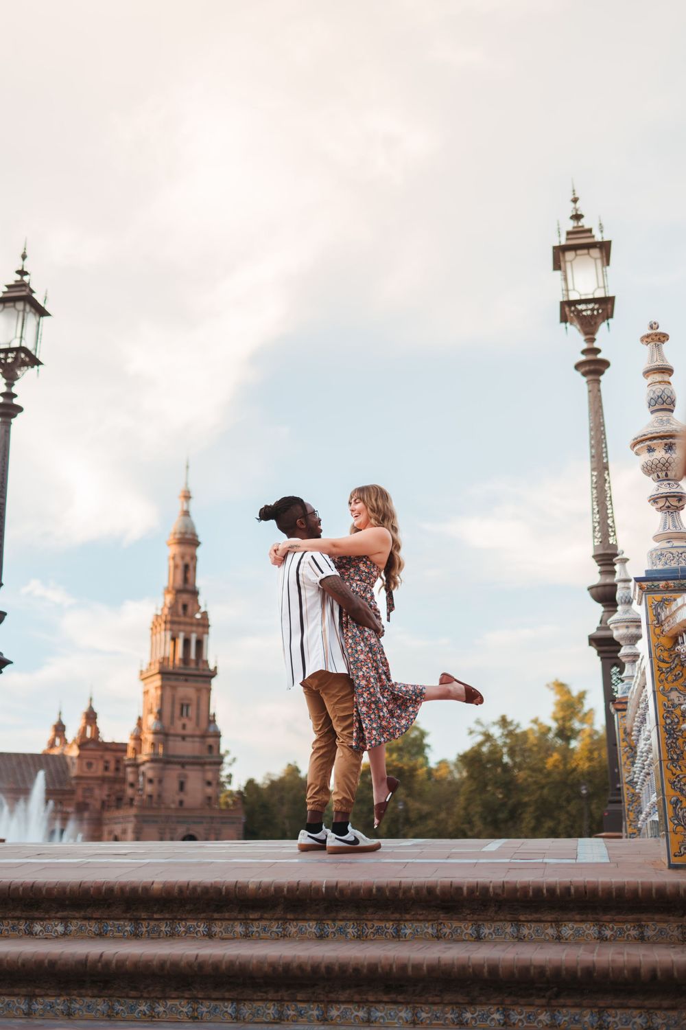 Joyful lift pose against Plaza de España's iconic towers and vintage lampposts.