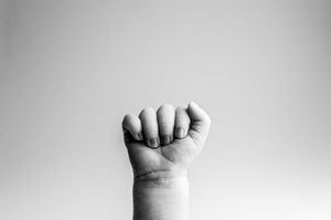 Black and white close-up photo of a clenched human fist with a plain background.