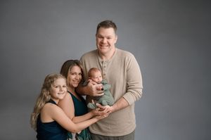 Family of four sitting close together and smiling during a professional studio portrait session.