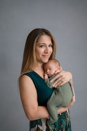 A parent in a teal sleeveless top embraces and snuggles with a small child wearing green against a gray background.