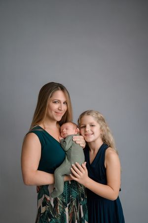 Family portrait in a studio with coordinated outfits in green and navy against a gray backdrop.