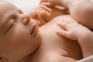 Close-up artistic photograph of a baby's face and hand with soft, dreamy lighting and neutral skin tones.