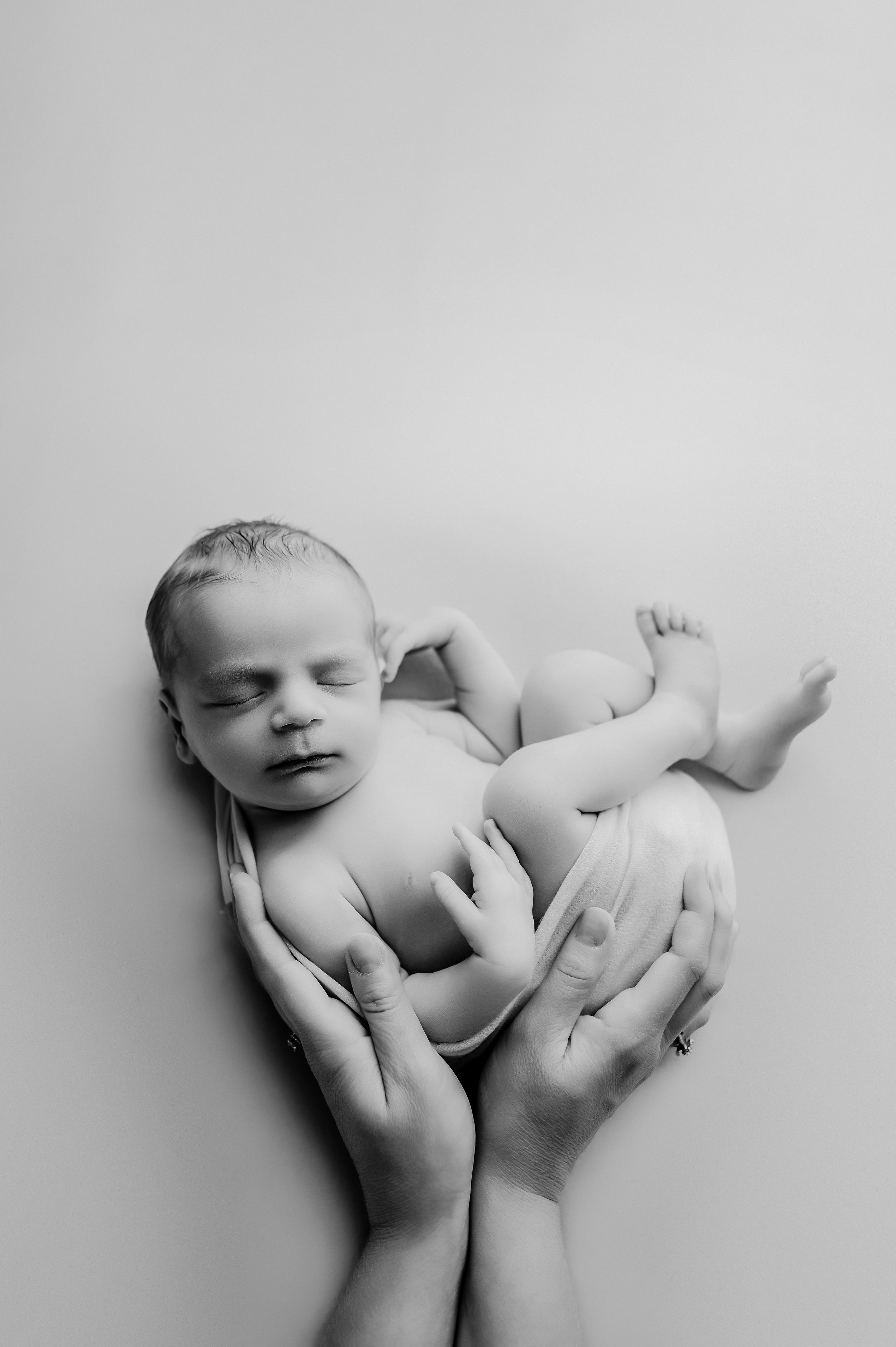 High contrast black and white close-up image of a baby's delicate sleeping face and hands.