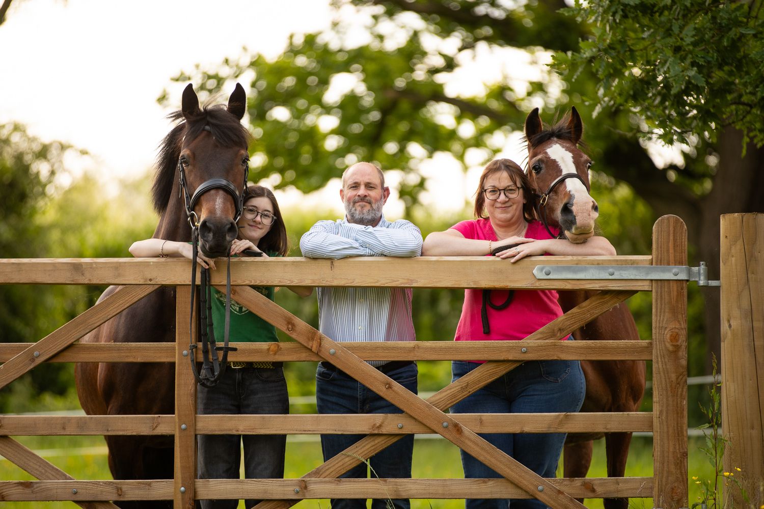 A group poses with horses along a tree-lined path during a sunny autumn day for outdoor photos.