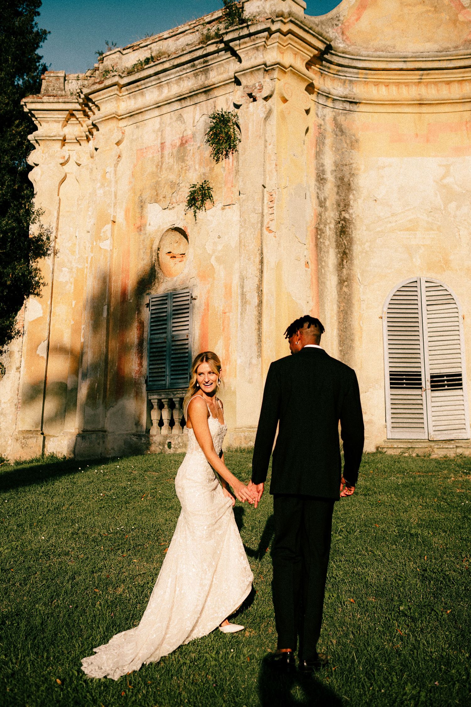 A couple poses playfully in a series of shots against a historic stone building with green lawn and blue sky.