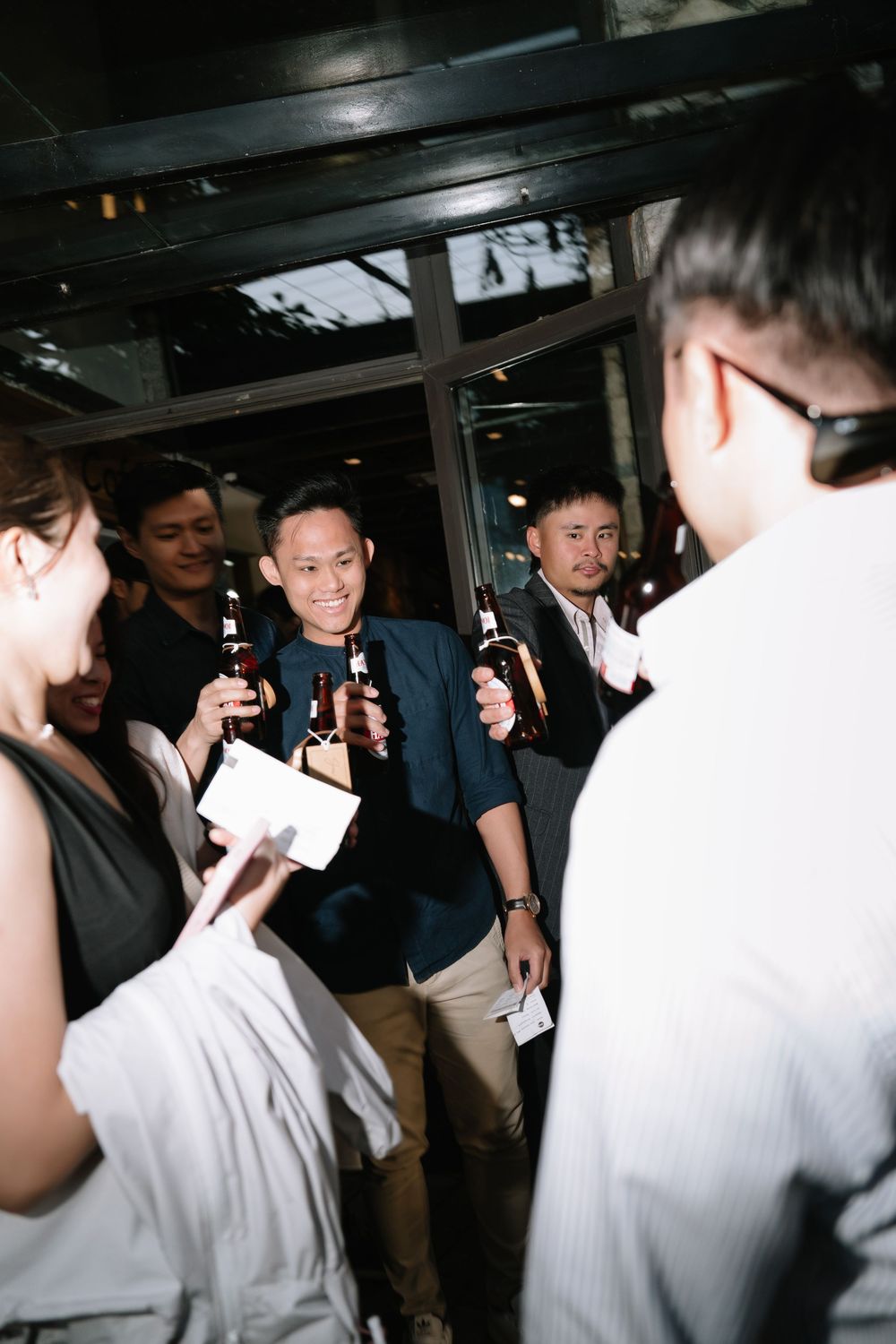 Group of young Asian men smiling and holding beer bottles at a nighttime social gathering.