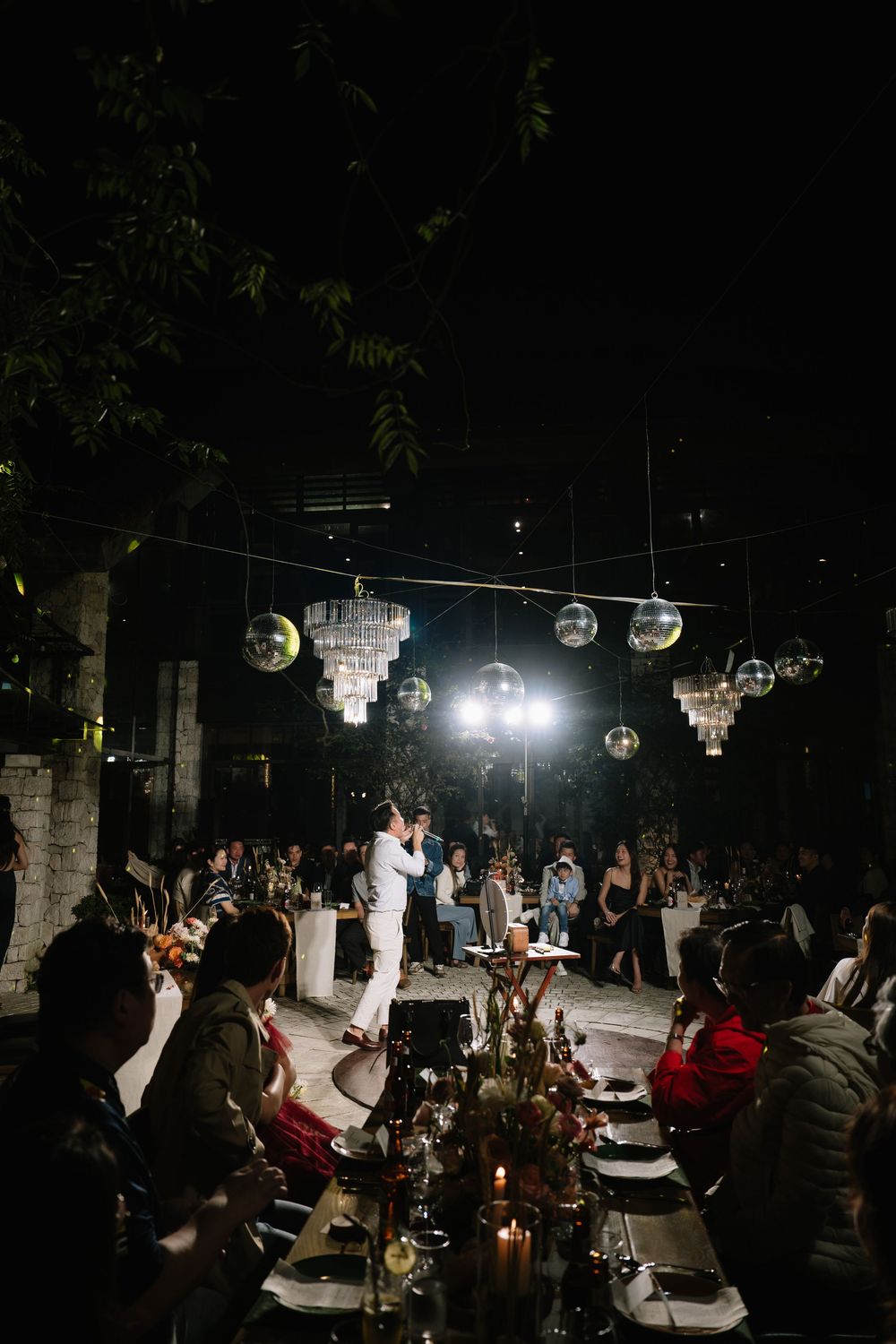 Elegant outdoor wedding reception at night with disco ball chandeliers and candlelit dining tables.