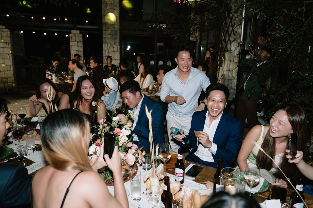 Joyful wedding guests laughing and celebrating together at an outdoor floral dinner reception.