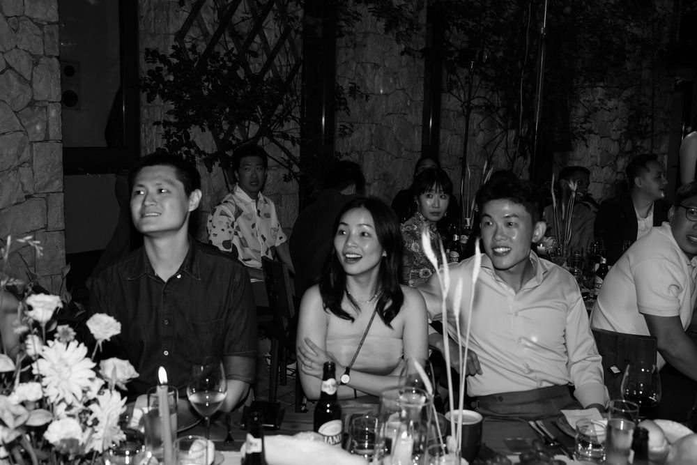 Black and white photo of three smiling guests seated at a candlelit wedding reception table.