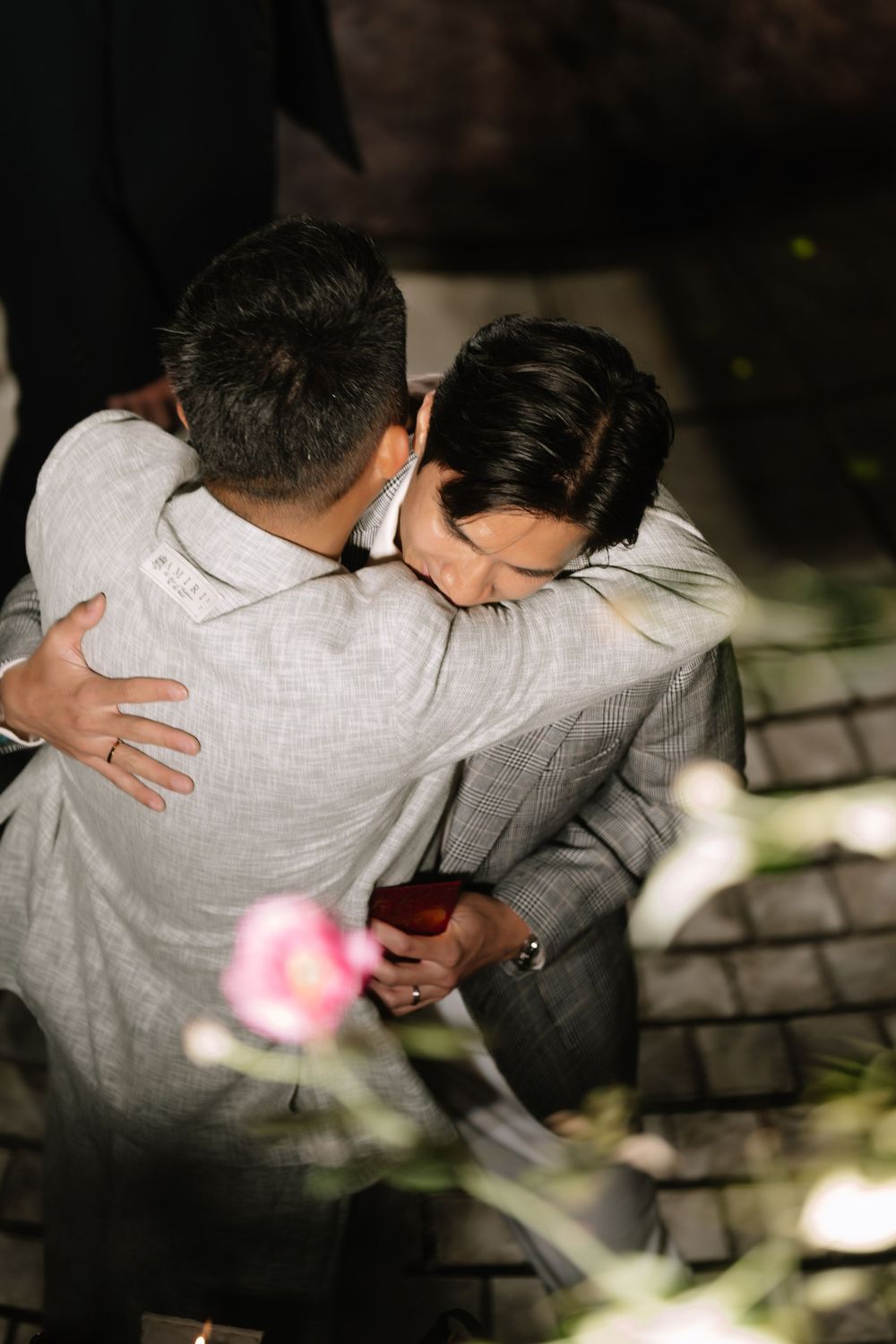 Two men sharing a warm embrace at an outdoor evening wedding celebration.