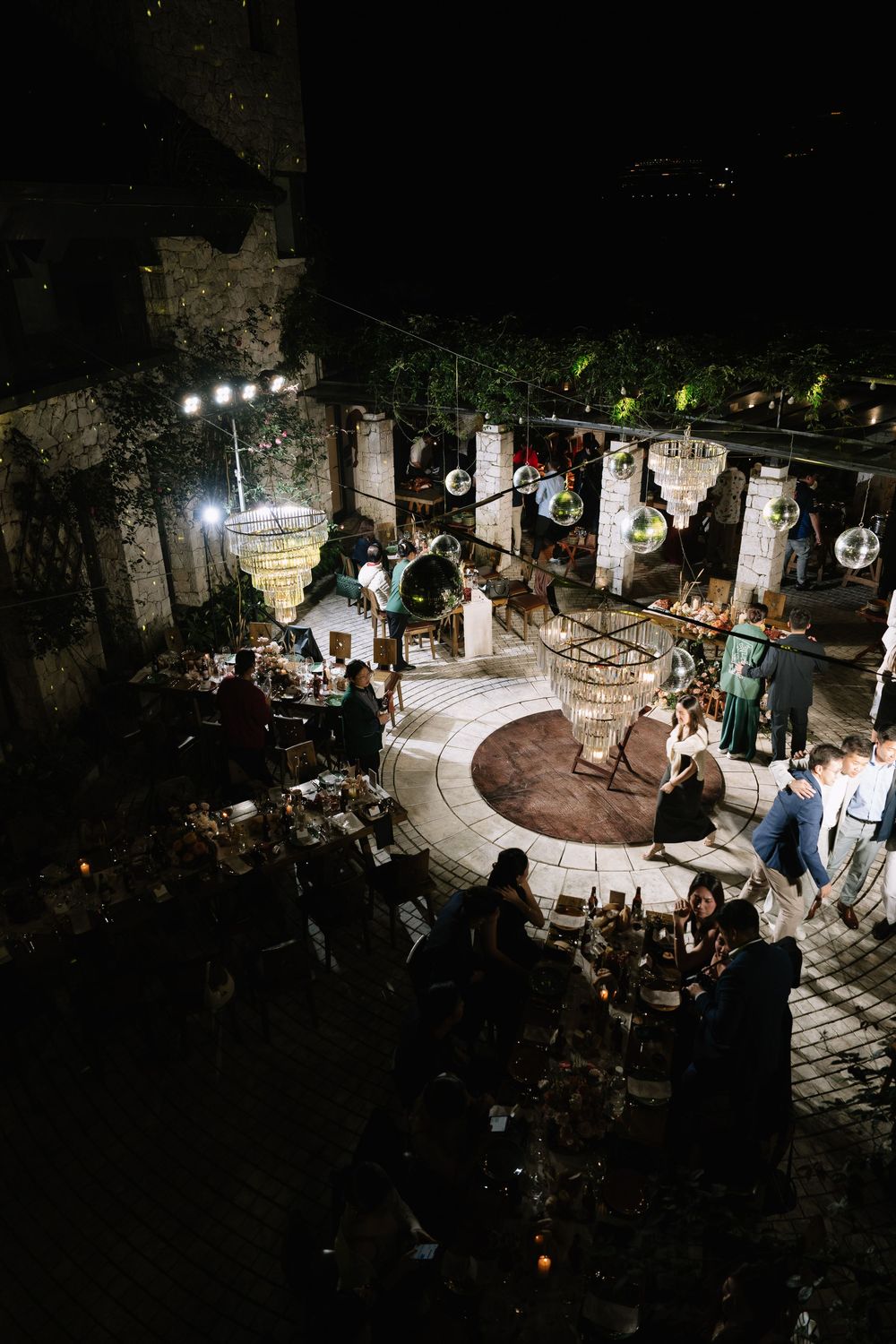 Aerial view of elegant outdoor wedding venue at night with chandeliers and circular dance floor.