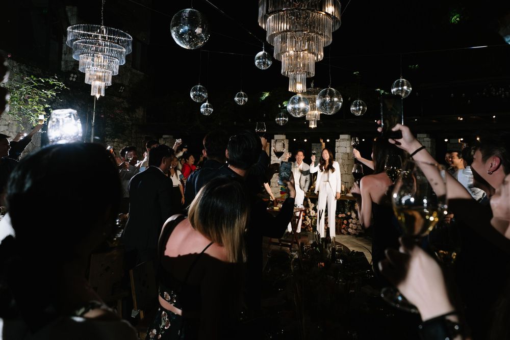 Crowd celebrating at a glamorous nighttime wedding reception with disco balls and chandeliers.