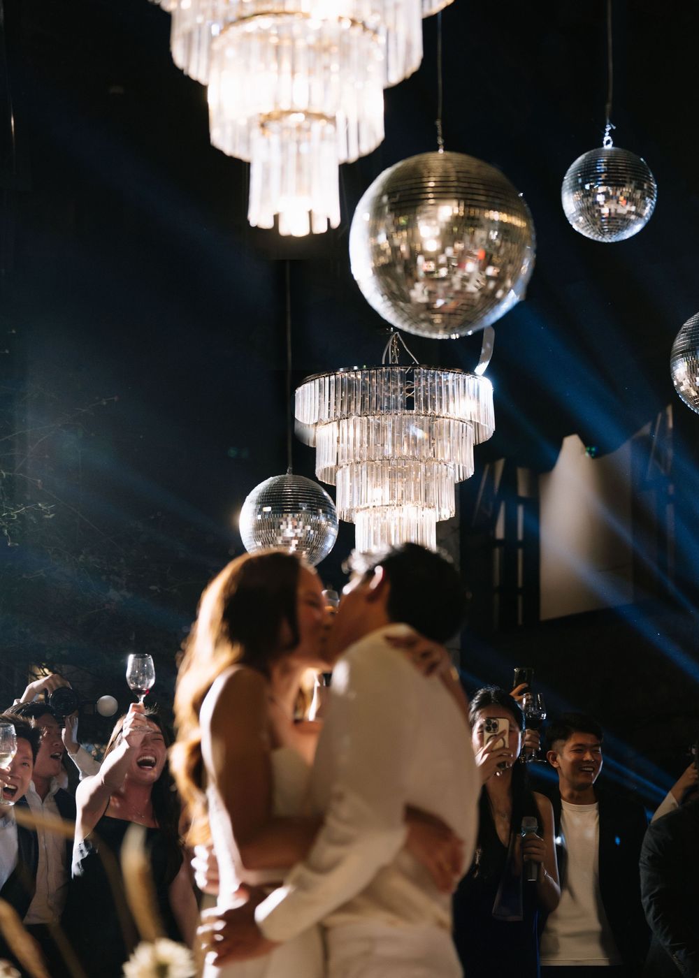 Newlyweds sharing a romantic kiss under glittering disco balls and chandeliers at their wedding.