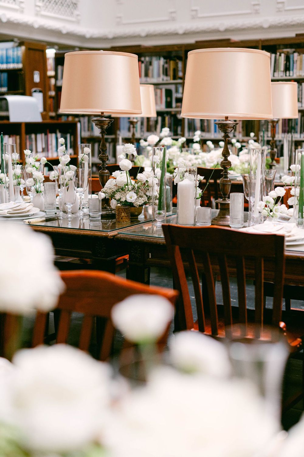 Elegant library reception setup with warm lighting and place settings at wooden tables.