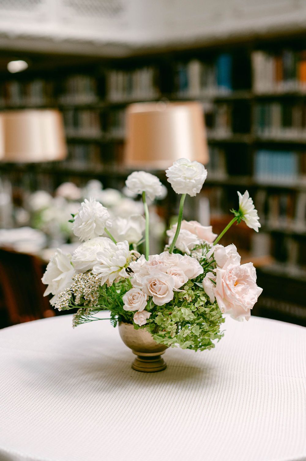 A romantic floral arrangement of pink roses, white flowers and greenery laid elegantly on a white tablecloth.
