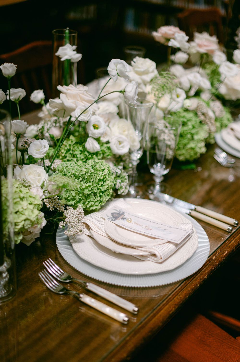 Elegant table setting with white plates, silver cutlery, and fresh floral centerpieces on dark wood tables.