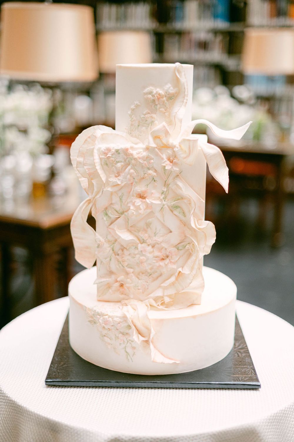 A series of white wedding cakes with delicate ruffled fondant designs displayed on black stands.