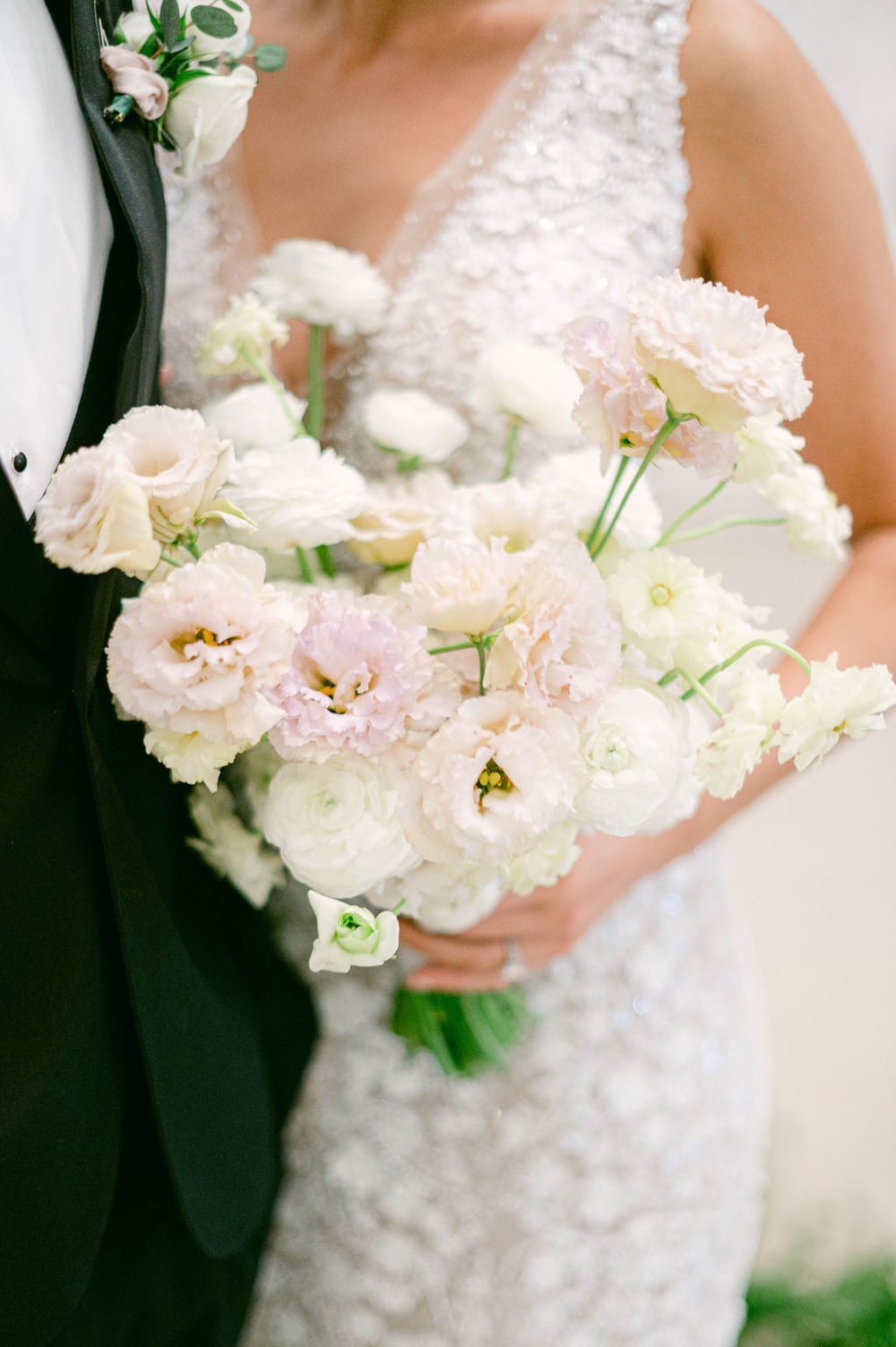 Close-up of delicate white and blush wedding bouquet with roses and lisianthus flowers against a bride's lace dress.
