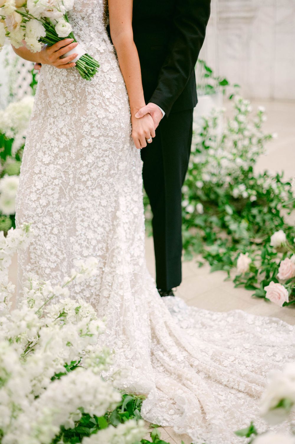 Close-up details of a sparkly sequined wedding dress train against a white backdrop with greenery.