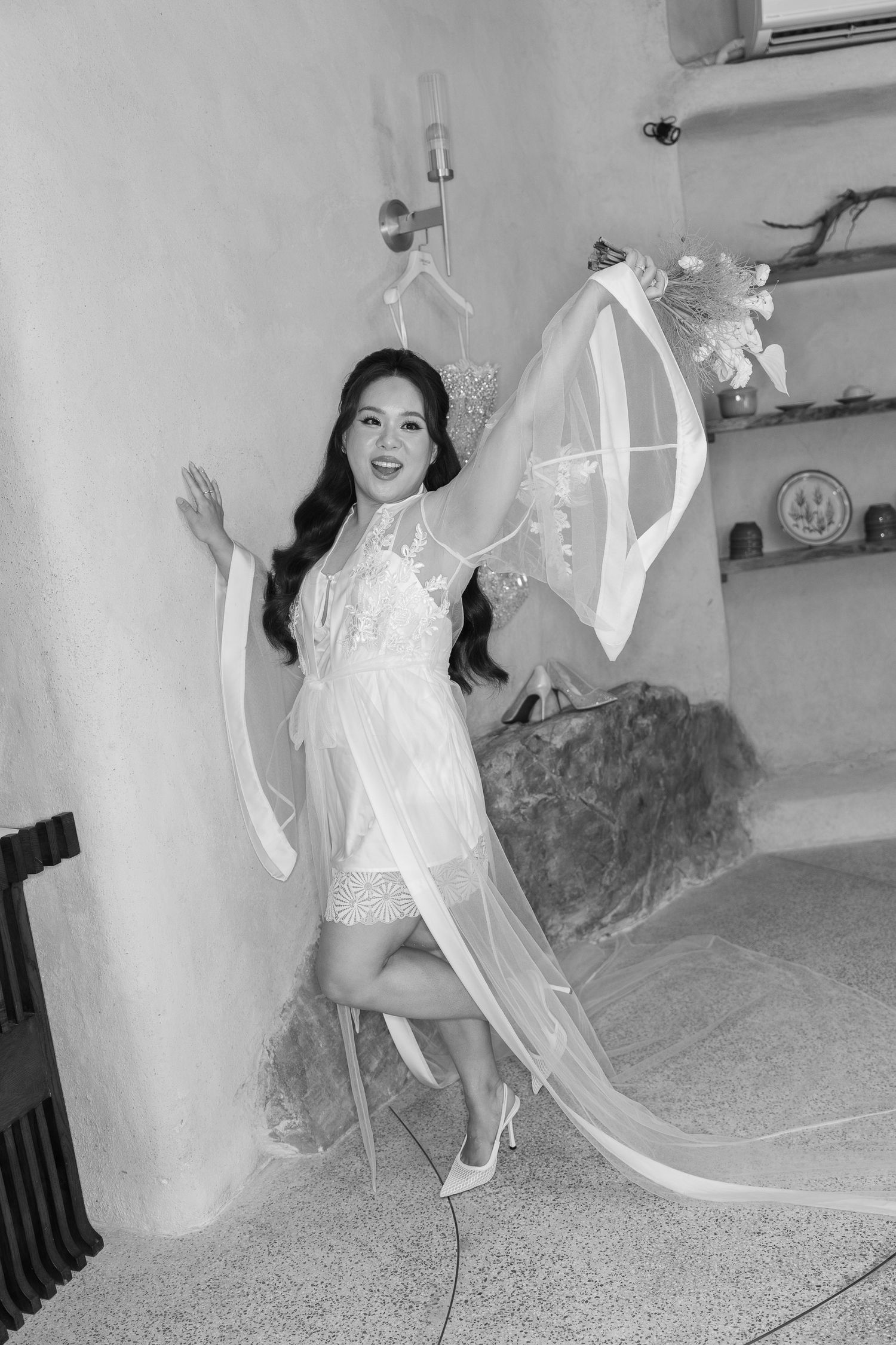 Black and white photo of bride in sheer white robe twirling with veil in a rustic room.