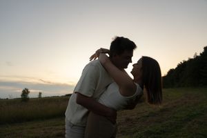 Intimate silhouettes embrace against a dusky sky in a peaceful countryside setting.