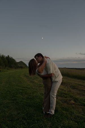 A couple shares tender moments in a grassy field under an evening sky.