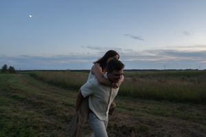 Two people stand close together in a field at dusk with a bright star overhead.