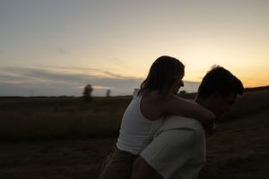 Silhouettes embrace against a warm sunset sky in a peaceful rural setting.