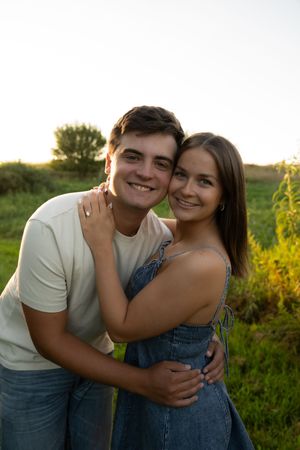 A couple poses together in a field during golden hour wearing casual summer outfits.